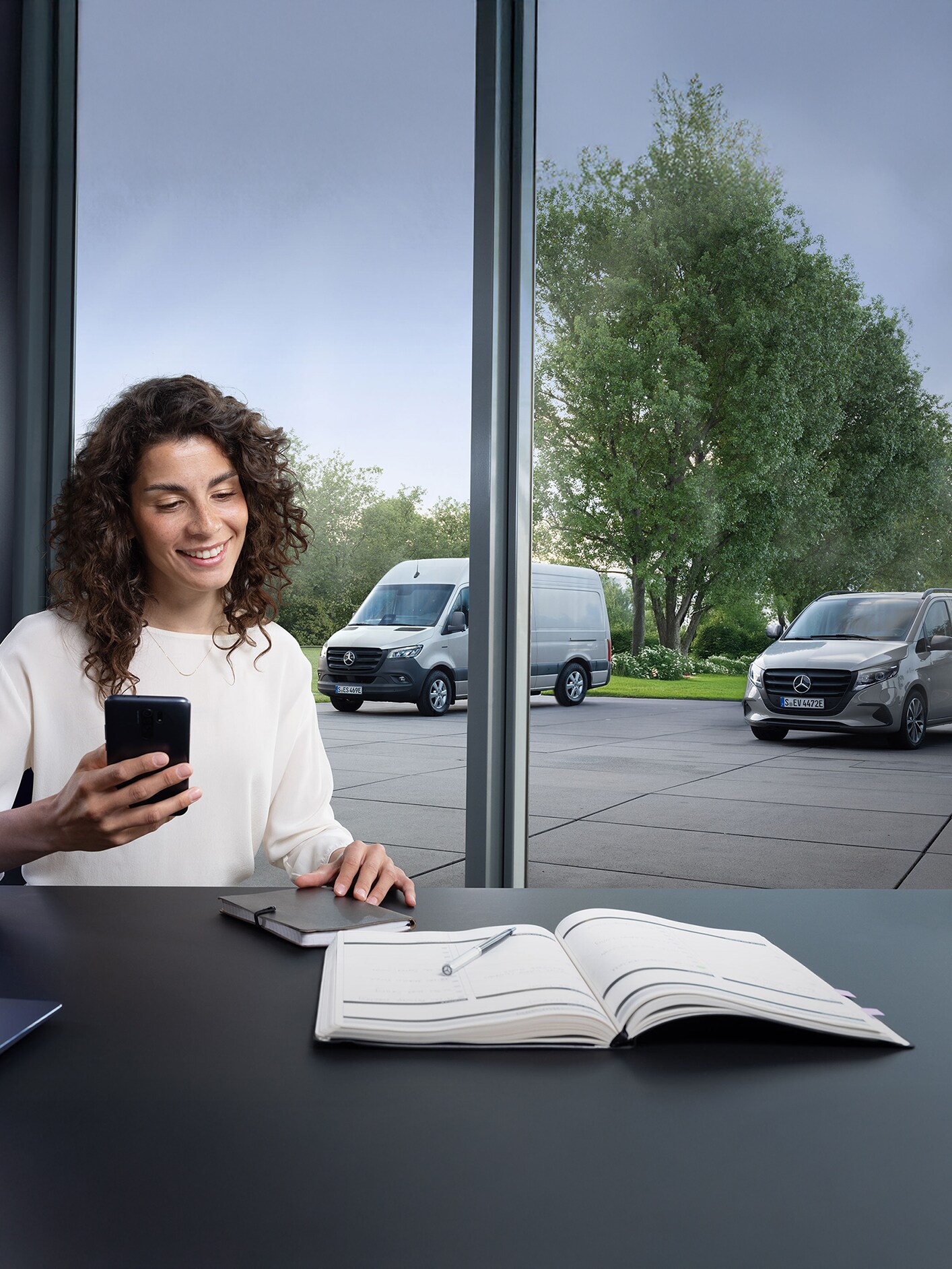 Arka planda çok sayıda Mercedes-Benz hafif ticari araç ile bir kadın akıllı telefonla servis randevusu alıyor.