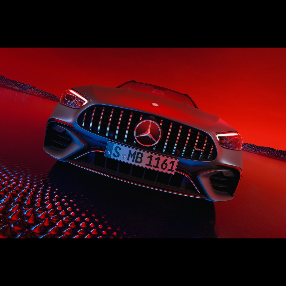 Kırmızı bir arka planın önünde duran Mercedes-AMG C 63 S E PERFORMANCE'ın önden görünümü.