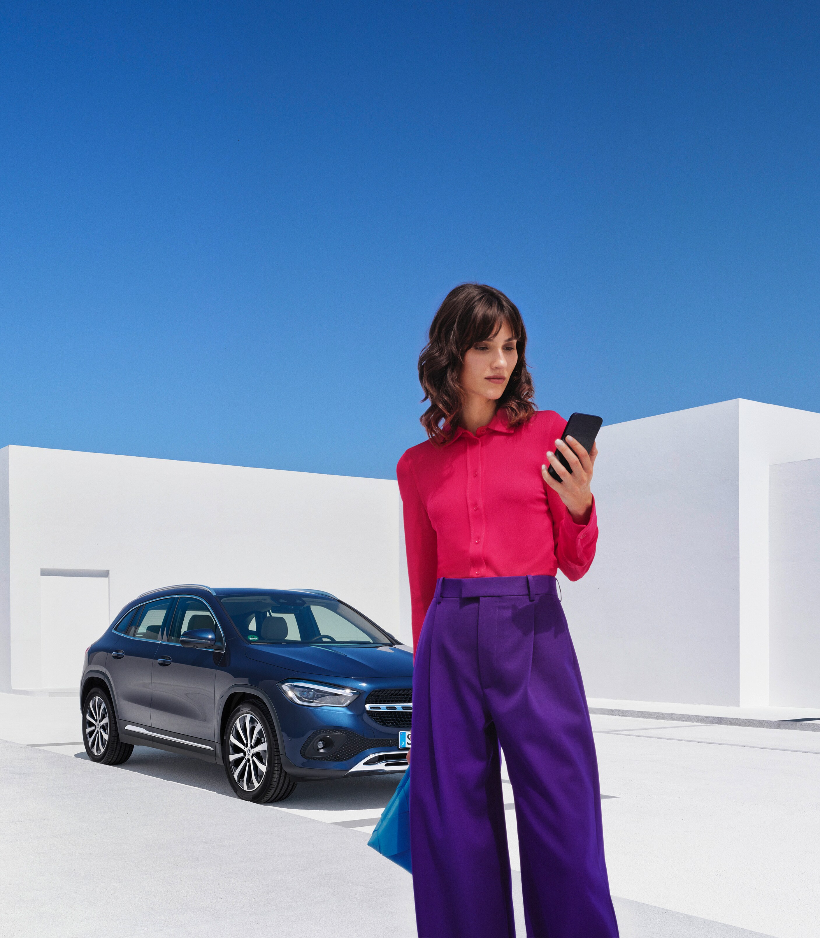 Bir kadın Mercedes-Benz aracının önünde duruyor ve akıllı telefonuna bakıyor.
