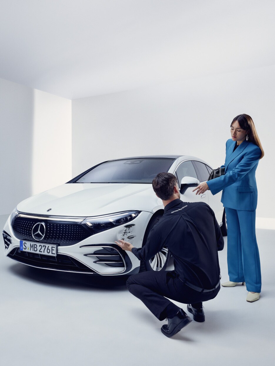 Hasarlı bir Mercedes-Benz'in yanında diz çöken Mercedes-Benz destek ekibinden bir adam