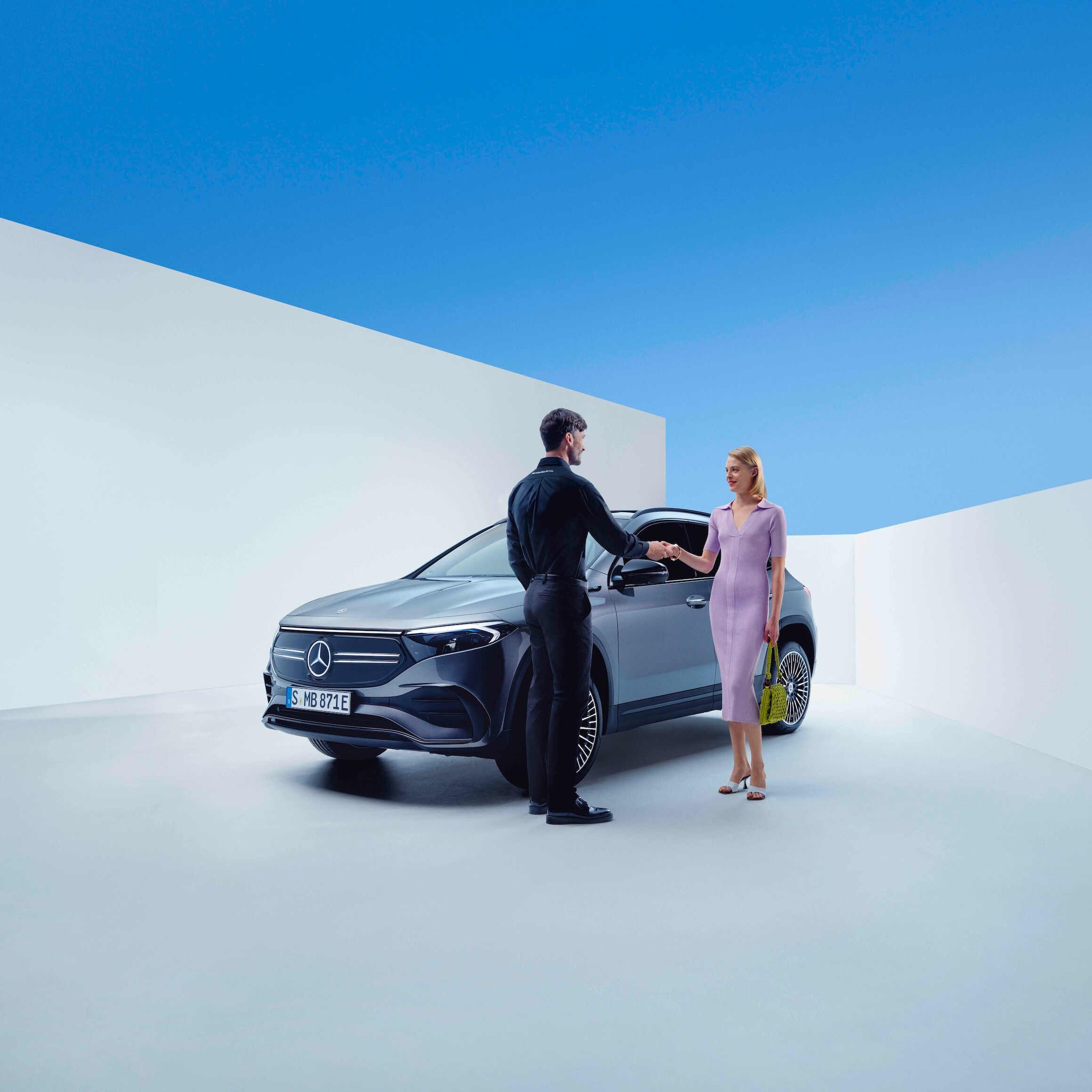 Bir Mercedes-Benz çalışanı ile bir kadın, bir Mercedes-Benz'in önünde el sıkışıyor