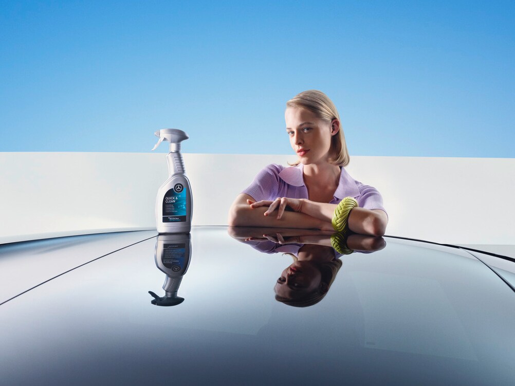 Bir kadın, temizlik ve yenileme donanımı ile bir Mercedes-Benz'e yaslanıyor.