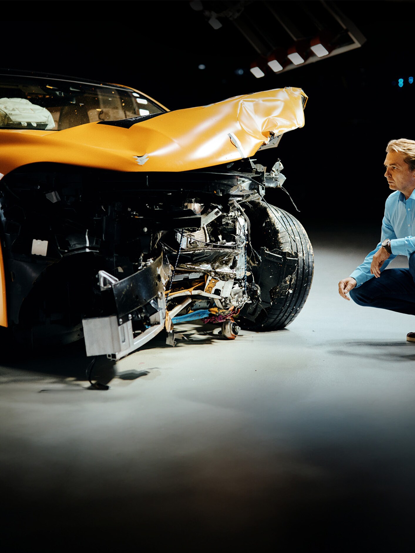 Çarpışma testi uzmanı, önden çarpan Mercedes-Benz aracı çömelerek inceliyor.