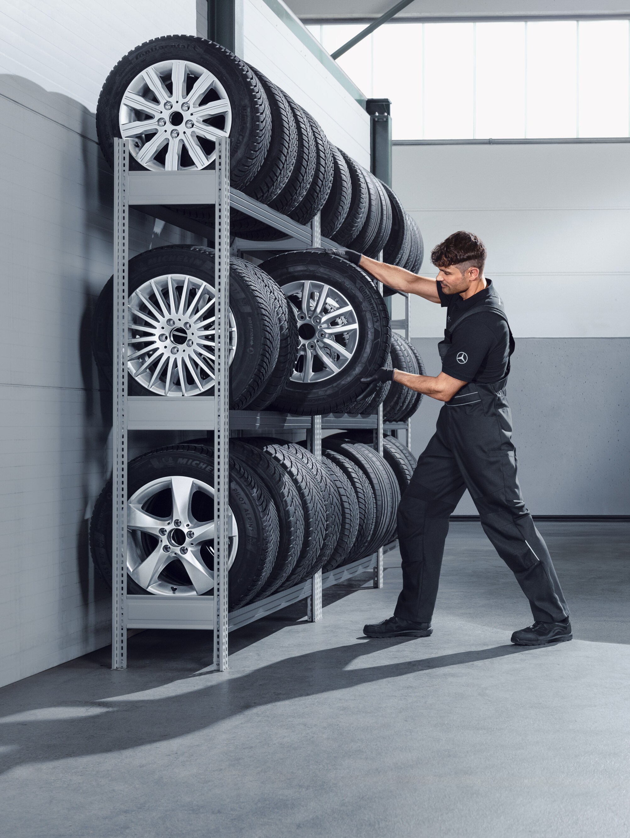 Beyaz bir Sprinter için servis rafından Mercedes-Benz komple kış lastikleri seçen bir mekanik teknisyeni.