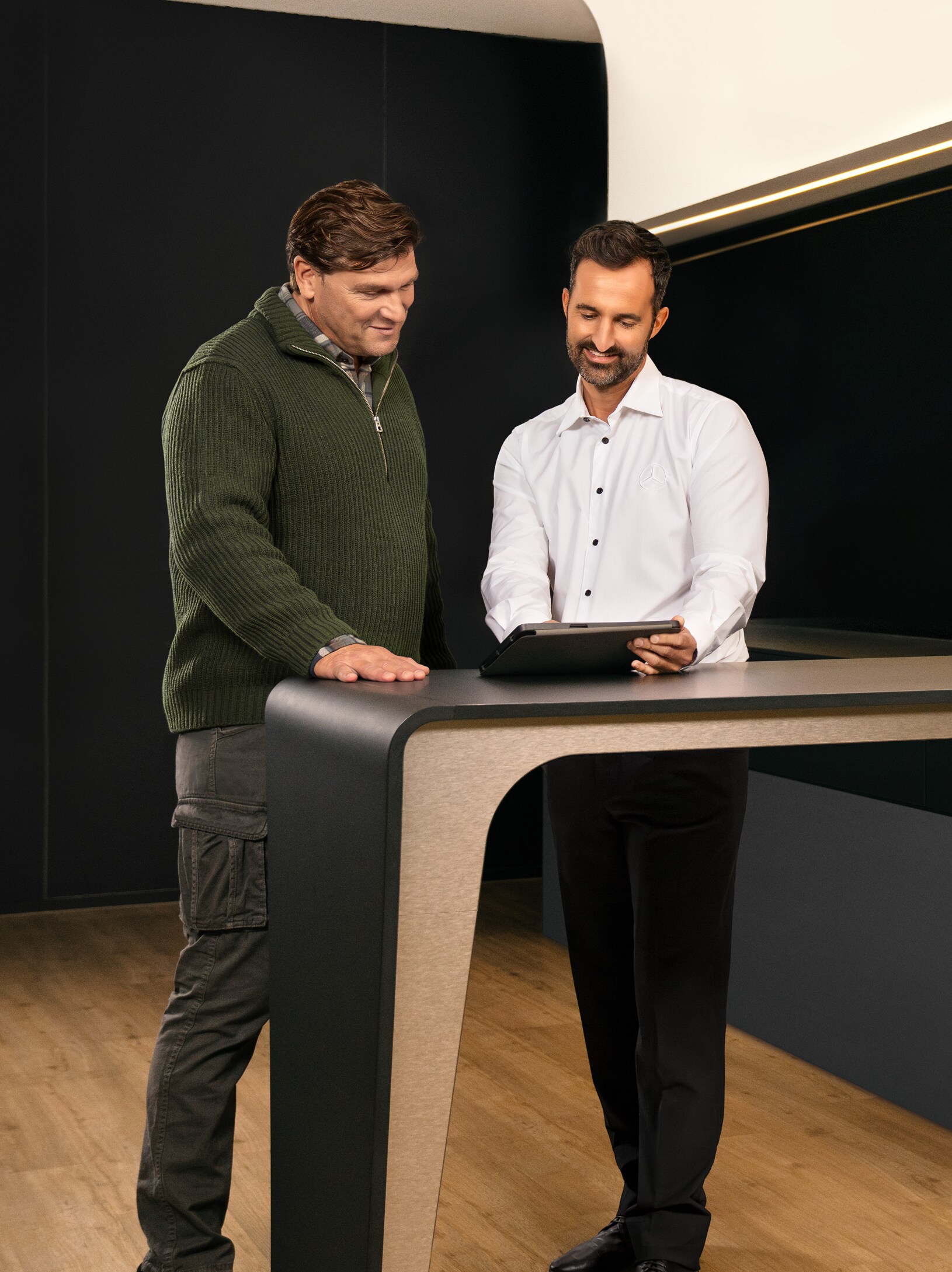 Masanın çevresinde duran iki kişi bir iPad'e bakarken fikir alışverişinde bulunuyorlar.