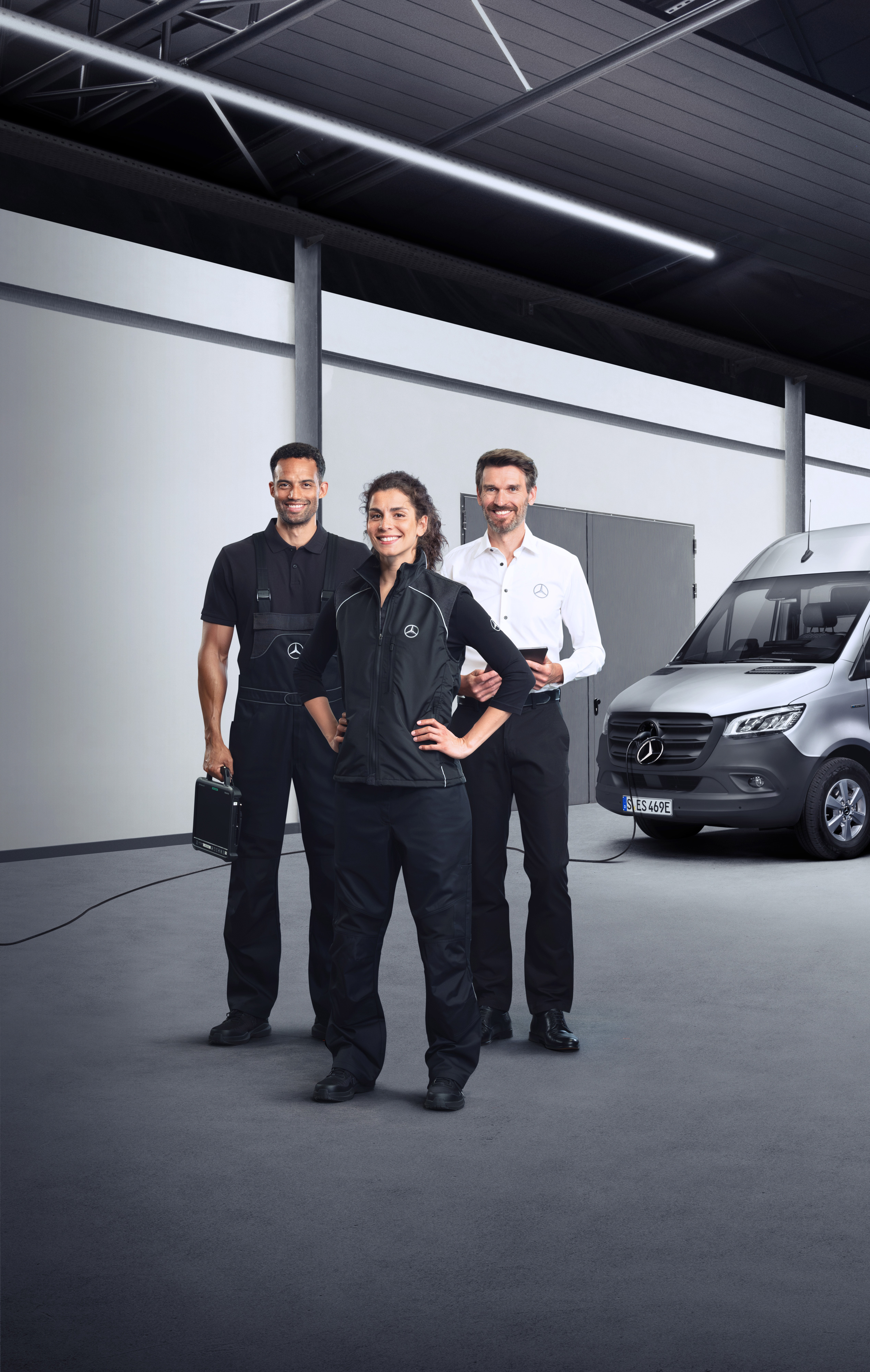 Mercedes-Benz | Hizmetlere Genel Bakış | Elektrikli Hafif Ticari Araç Servisleri Şarj kablosu takılı gümüş bir Mercedes-Benz eSprinter önünde duran üç personel.