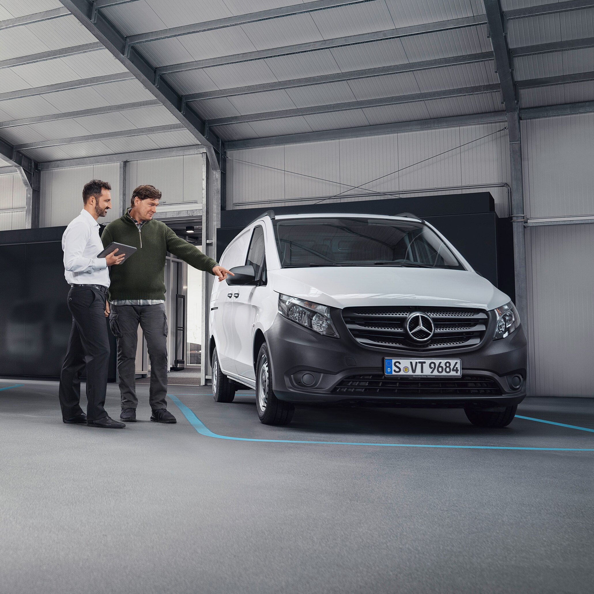 Mercedes-Benz müşteri destek temsilcisi, bir servis partneri lokasyonunda bir hafif ticari aracın önünde müşteriyle birlikte.